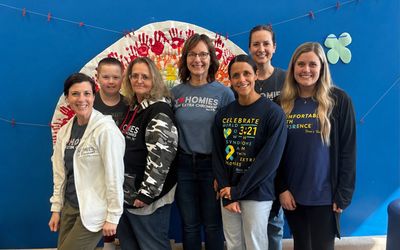 The Therapy Connections team standing together in front of a colorful handprint mural