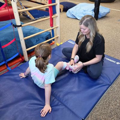 A physical therapist and a young girl stretching together on blue therapy mats